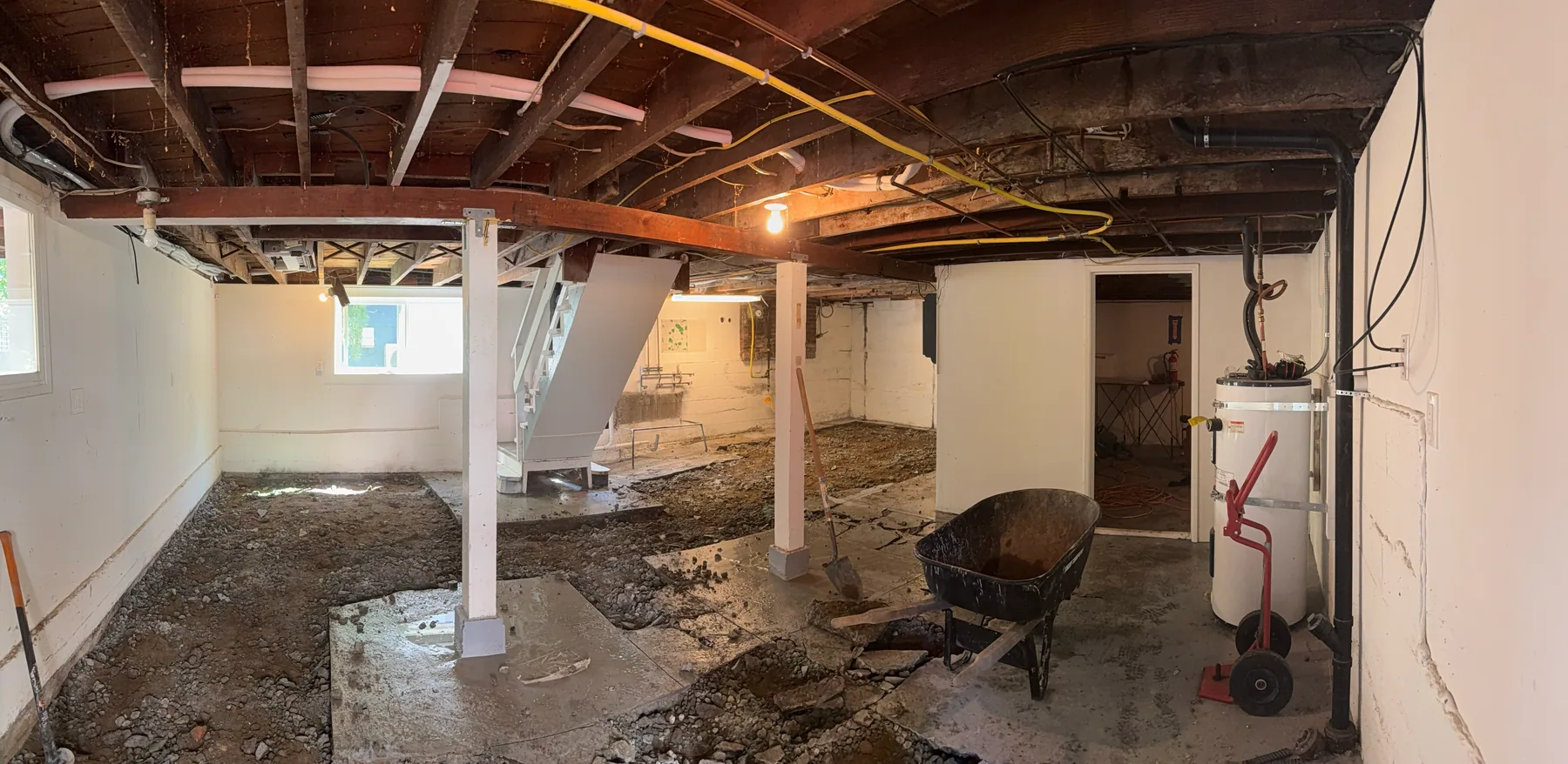 Basement floor opened in sections with loose concrete and a wheelbarrow in the work area