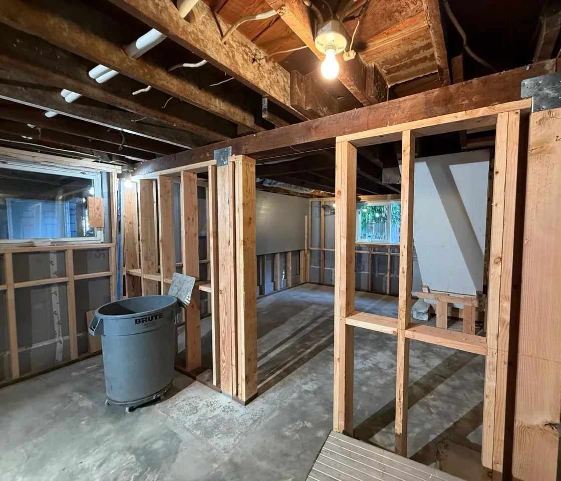 Completed basement wall framing forming room openings beside the smooth concrete slab
