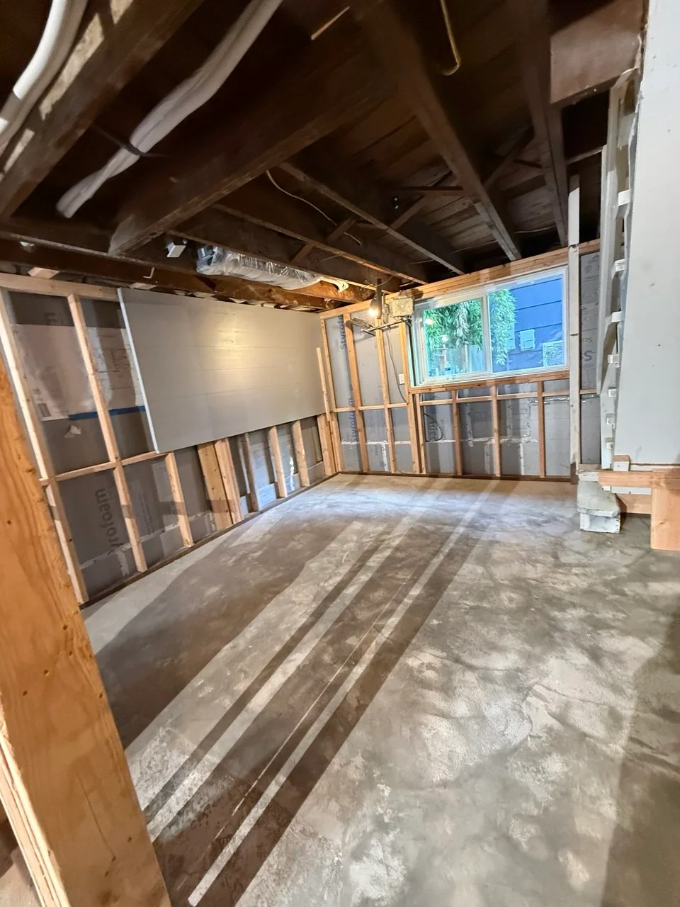 Open basement room with concrete floor, insulated perimeter framing and exposed ceiling joists