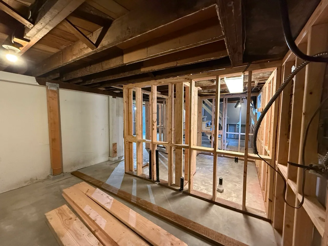 Completed partition wall framing with plumbing stubs and staged lumber in the foreground