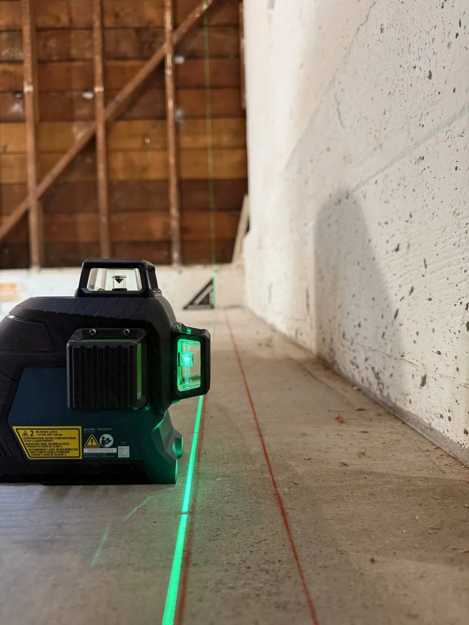 Green construction laser projecting a reference line across the new basement slab