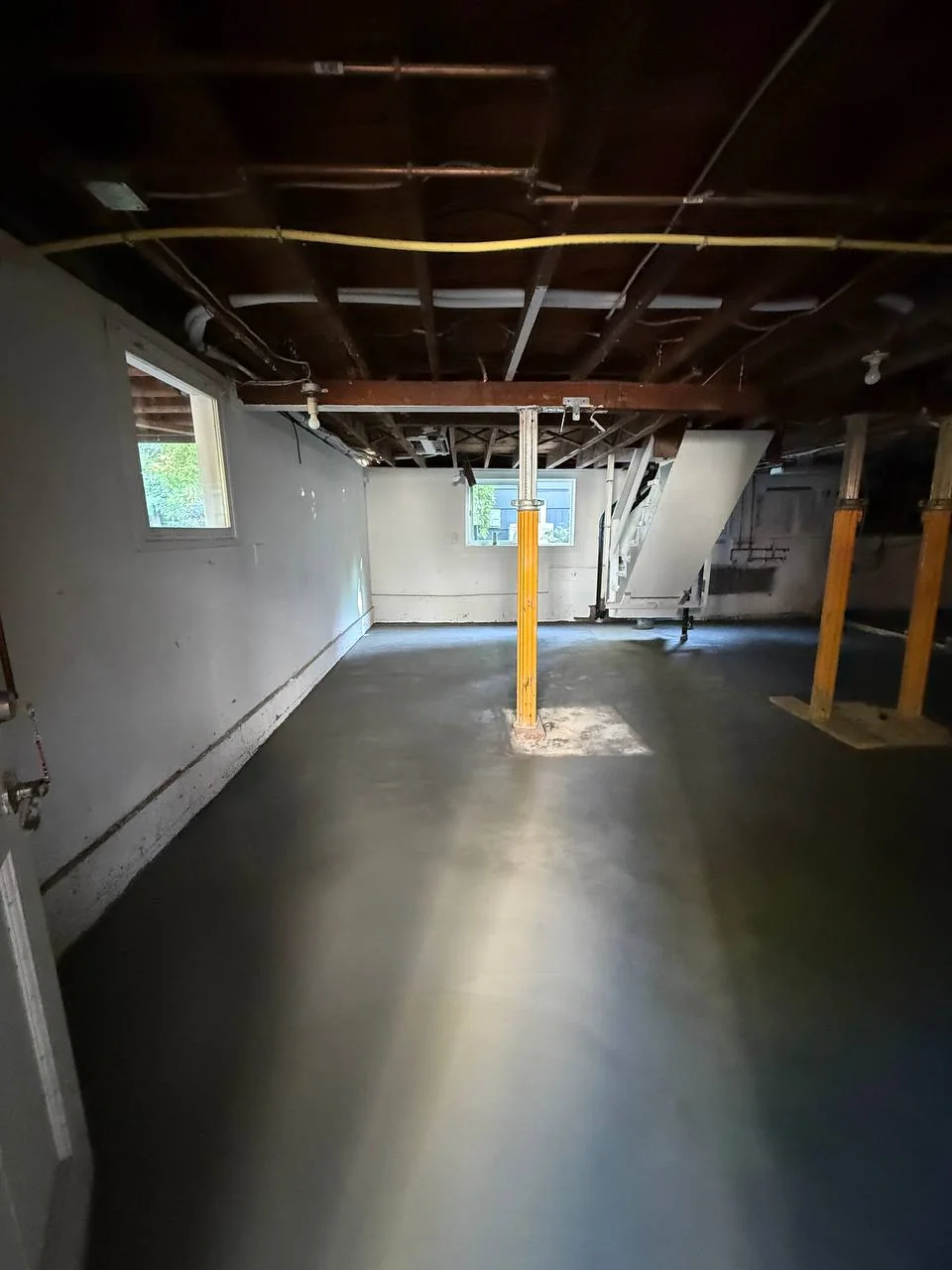 Lengthwise basement view showing the new concrete floor beneath exposed framing and temporary supports