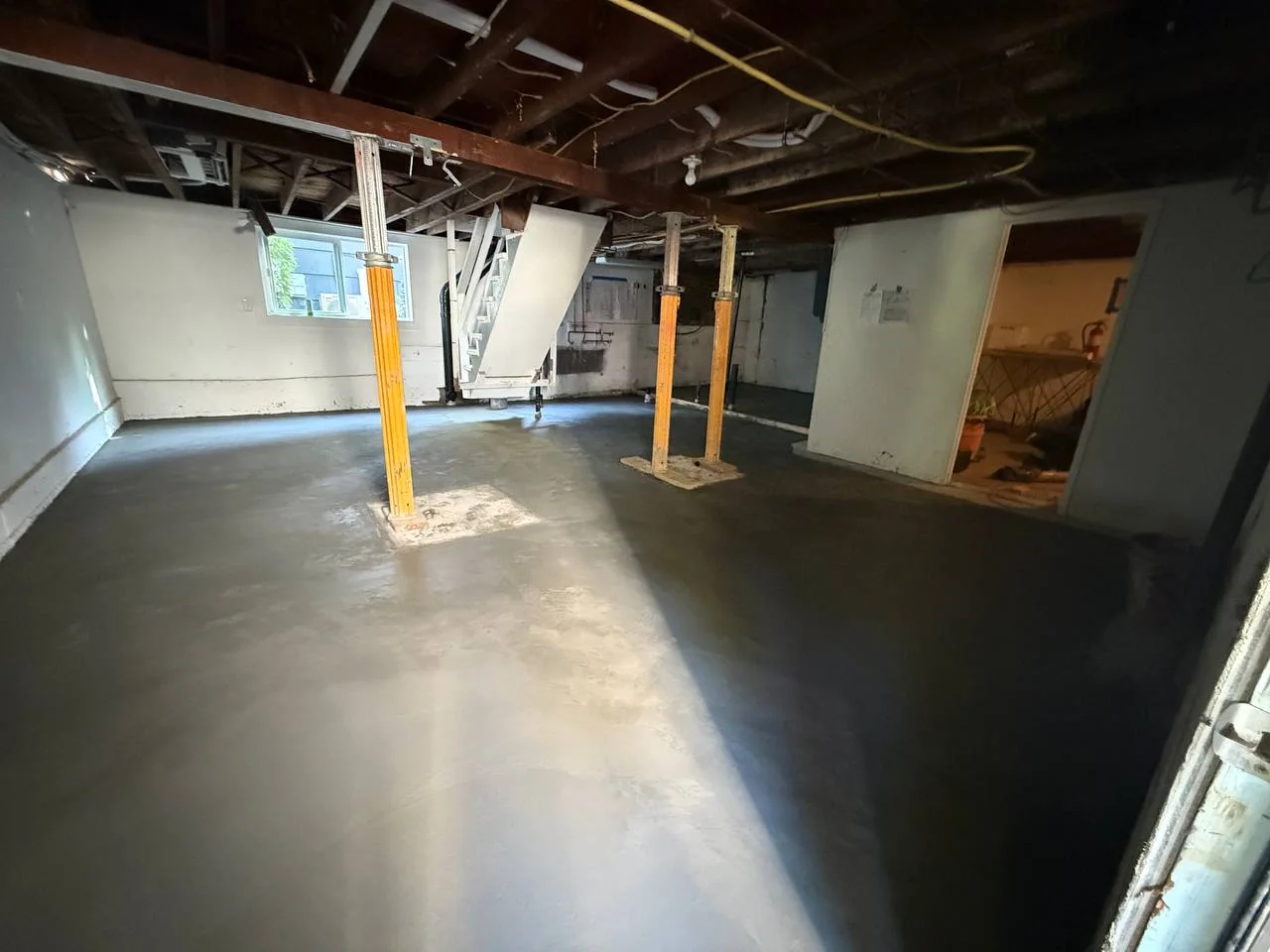 Wide basement view with a smooth newly placed concrete floor and temporary support posts