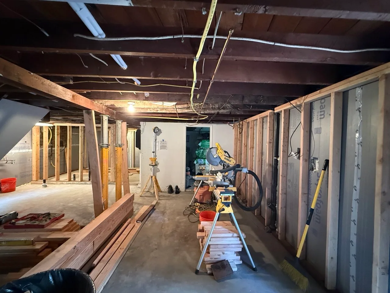 Pink rigid-foam insulation installed against basement exterior concrete walls beside new wood framing
