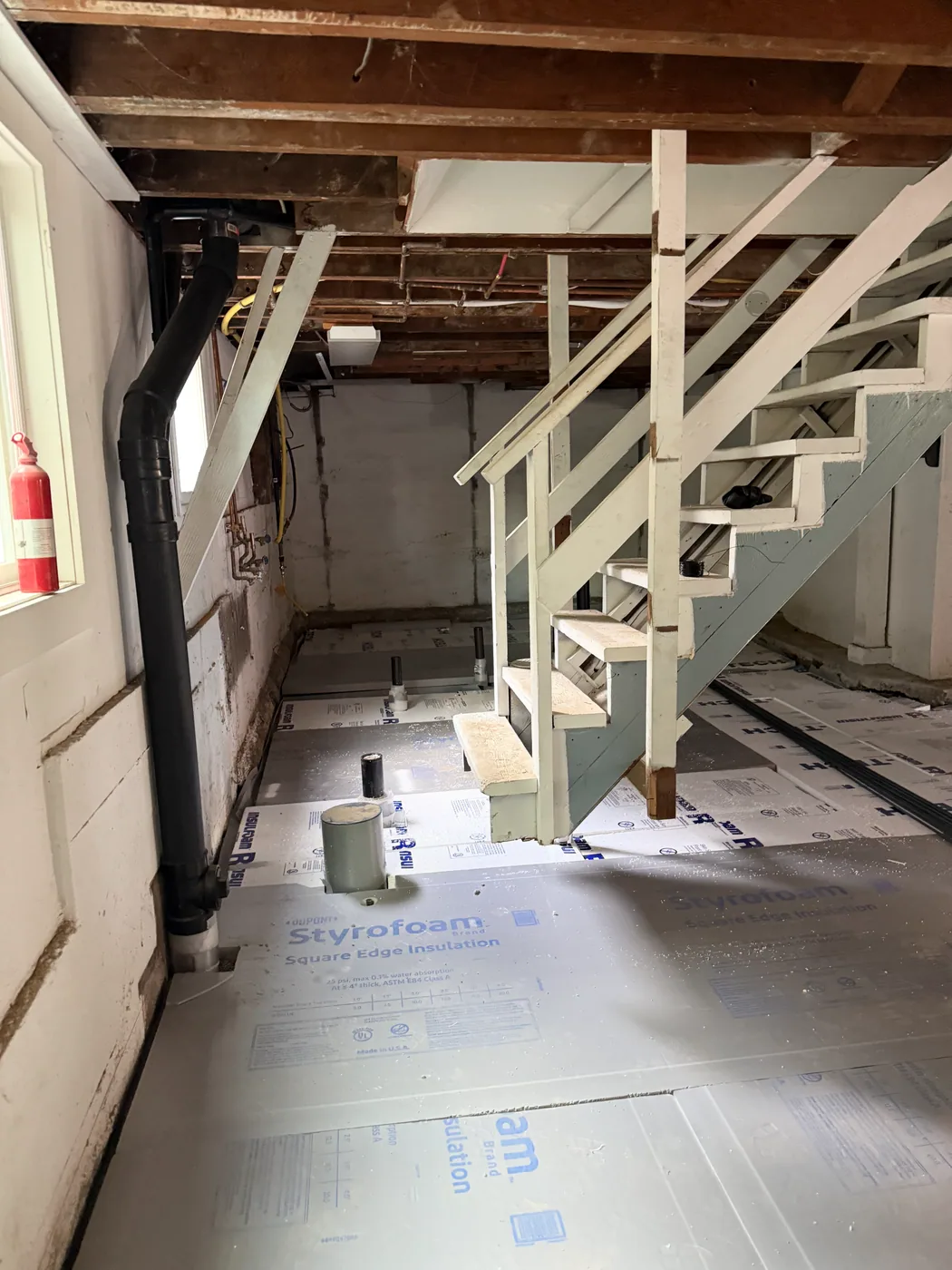 Rigid-insulation panels fitted around the basement stair and visible pipe penetrations