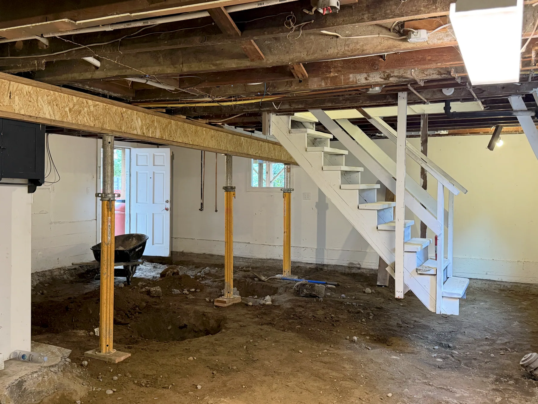 Basement with the concrete floor removed and yellow temporary support posts visible