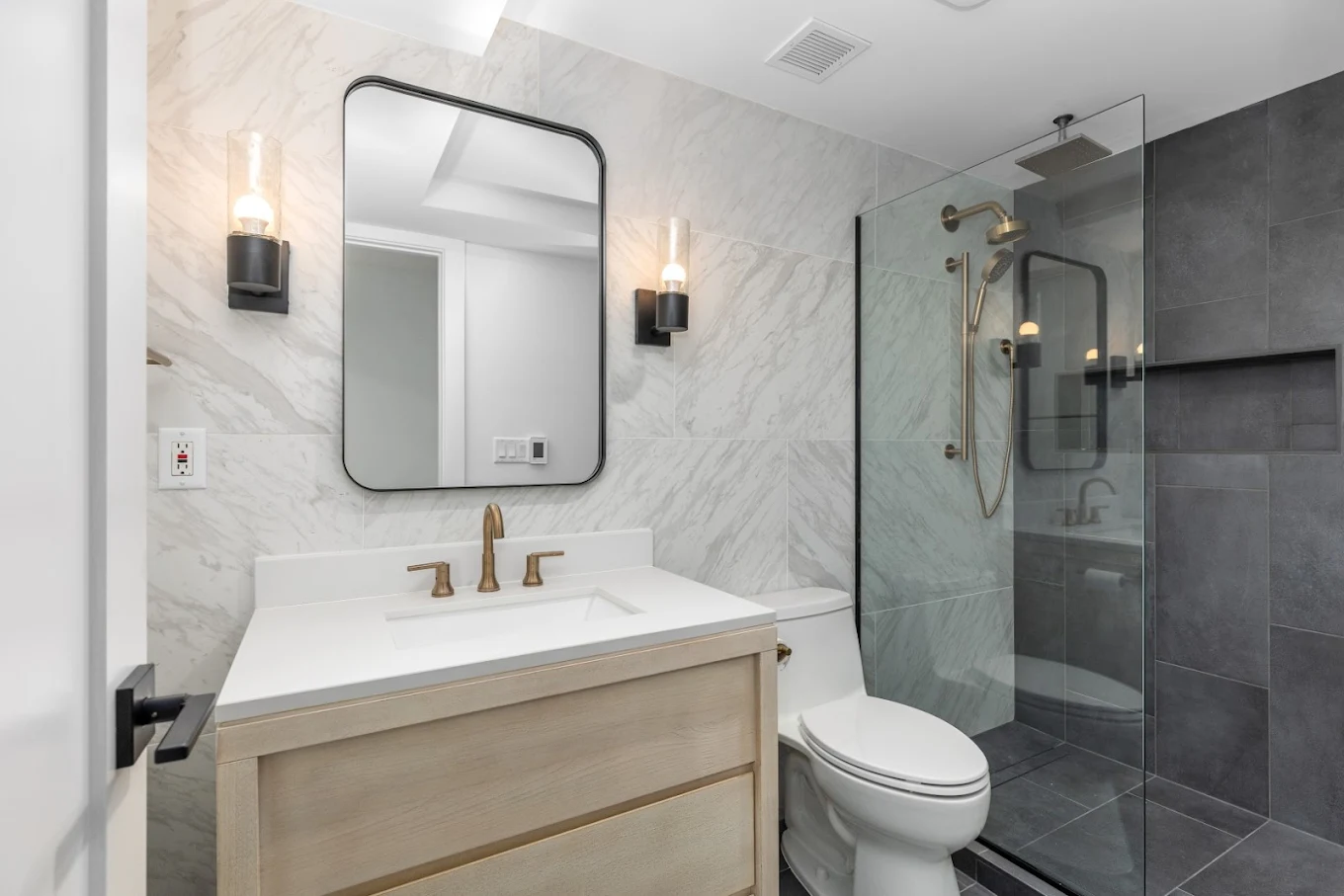 Remodeled bathroom with warm brass fixtures and charcoal shower tile